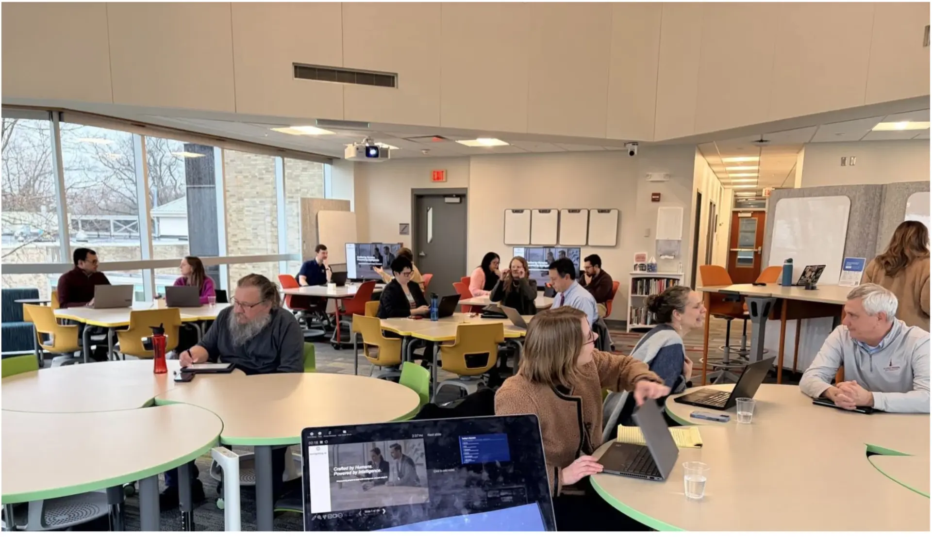 Teams working together in a navigating ai leadership and staff workshop, laptops open around round tables